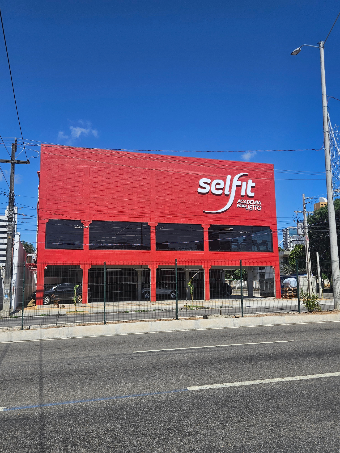 Fachada de academia Selfit em alvenaria vermelha com letreiro branco e estacionamento térreo